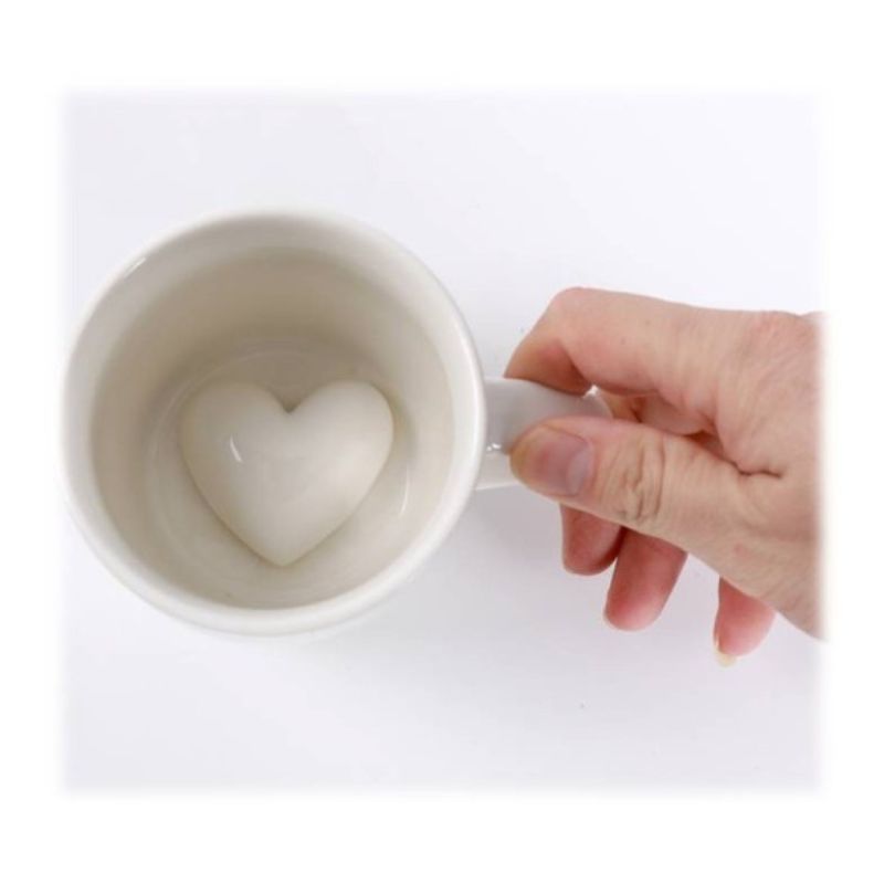 Caneca 3D com detalhe de coração no interior, segura por uma mão.