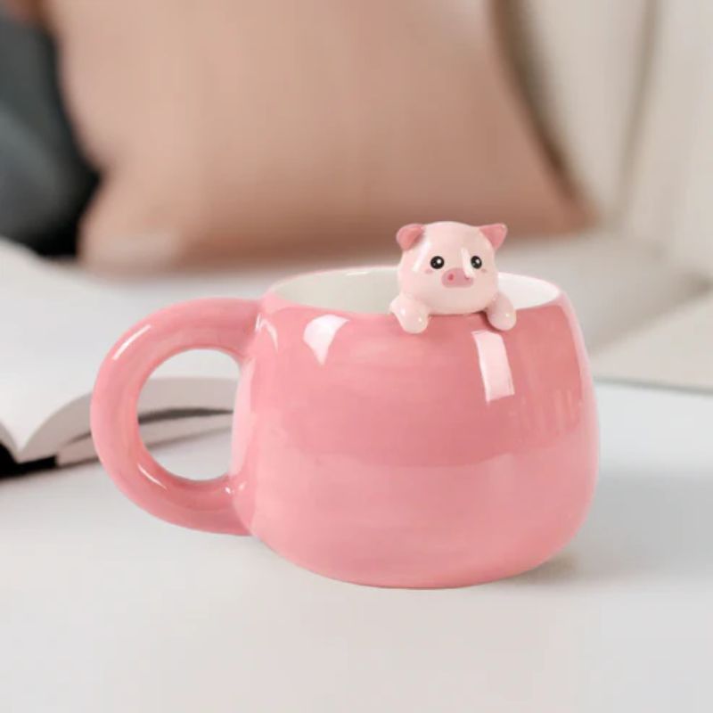 Caneca com porquinho usada como decoração sobre mesa branca, com almofadas ao fundo.