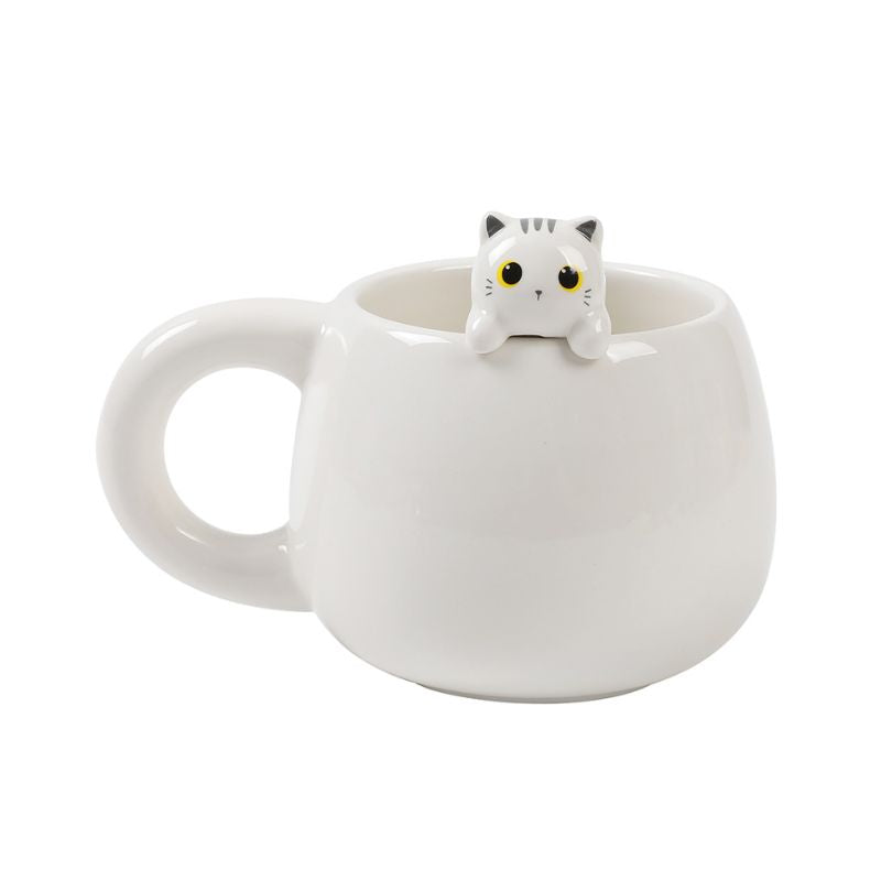Caneca branca com figura de gato no seu interior espreitando sobre a borda, vista de lado.