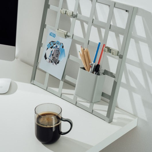 Conjunto de canetas sabres de luz Star Wars colocadas sobre uma secretária moderna com elementos de decoração e uma caneca de café ao lado.