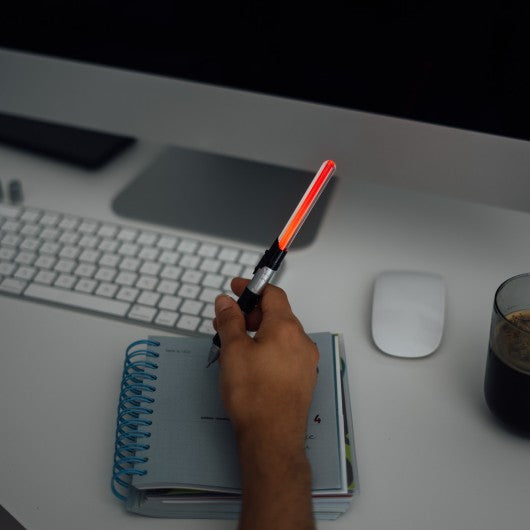 Utilização de uma caneta sabre de luz Star Wars com luz LED vermelha acesa num ambiente escuro, enquanto escreve num caderno.