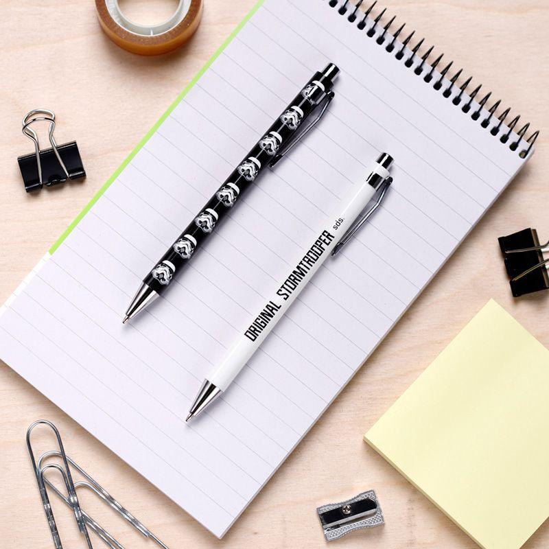Foto de uma mesa de trabalho com um conjunto de canetas Stormtrooper, uma preta e outra branca, sobre um caderno listrado, ilustrando o uso diário.
