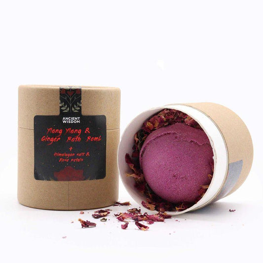 Embalagem cilíndrica de cartão com rótulo frontal exibindo o nome 'Ylang Ylang & Ginger Bath Bomb', com detalhes em rosa e preto.