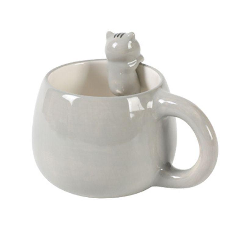 Caneca cinza com figura de gato no seu interior espreitando sobre a borda, vista de lado.