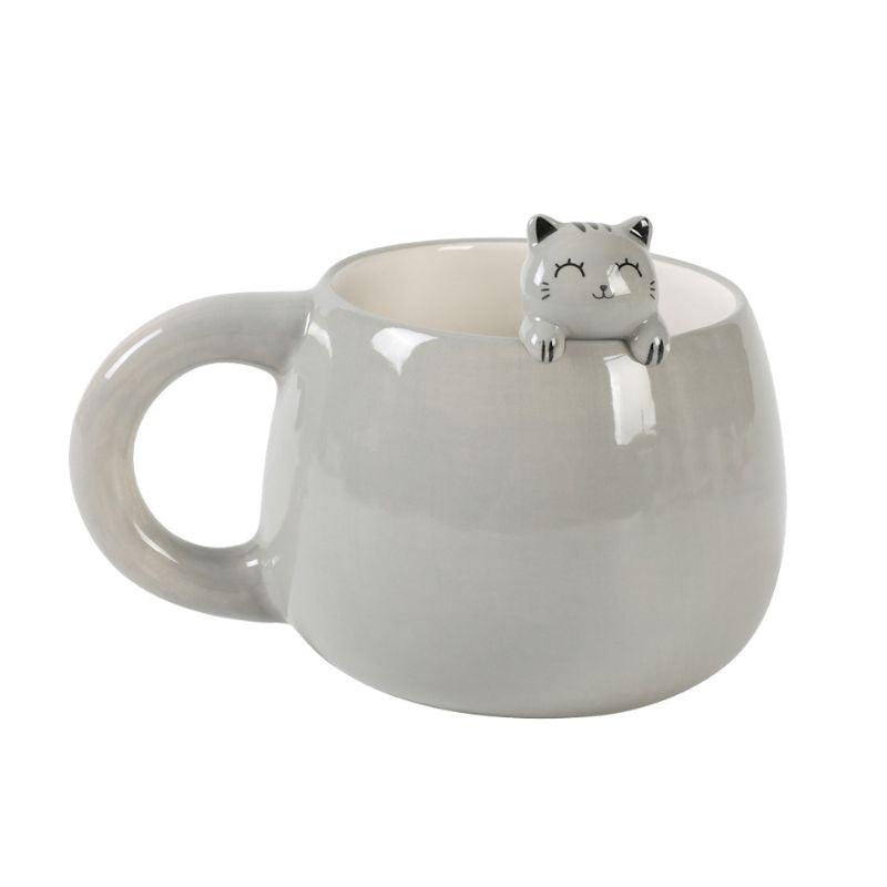 Caneca cinza com figura de gato sorridente de olhos fechados no seu interior espreitando sobre a borda.