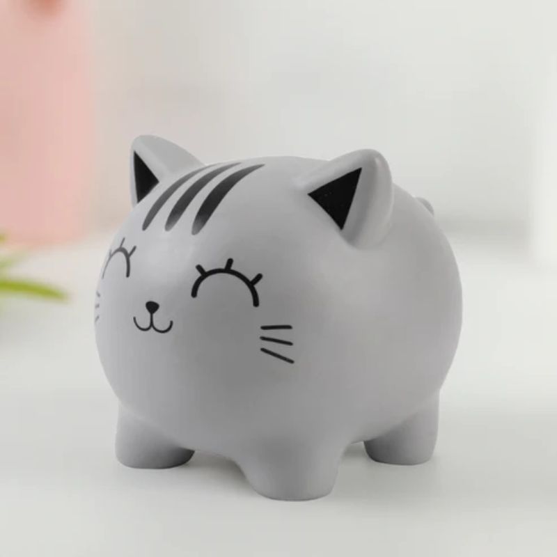 Mealheiro de gatinho cinzento usado como peça decorativa sobre superfície branca com fundo desfocado.