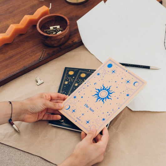 Pessoa a segurar o caderno "The Sun" do Pack Astral, destacando o design dourado inspirado no sol e cosmos.