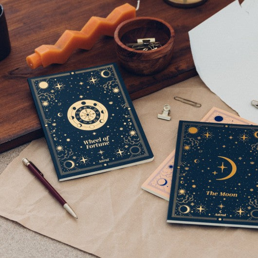 Pack 3 Cadernos A5 Astral decorados em ambiente elegante com o caderno "The Moon" e "Wheel of Fortune" em destaque.
